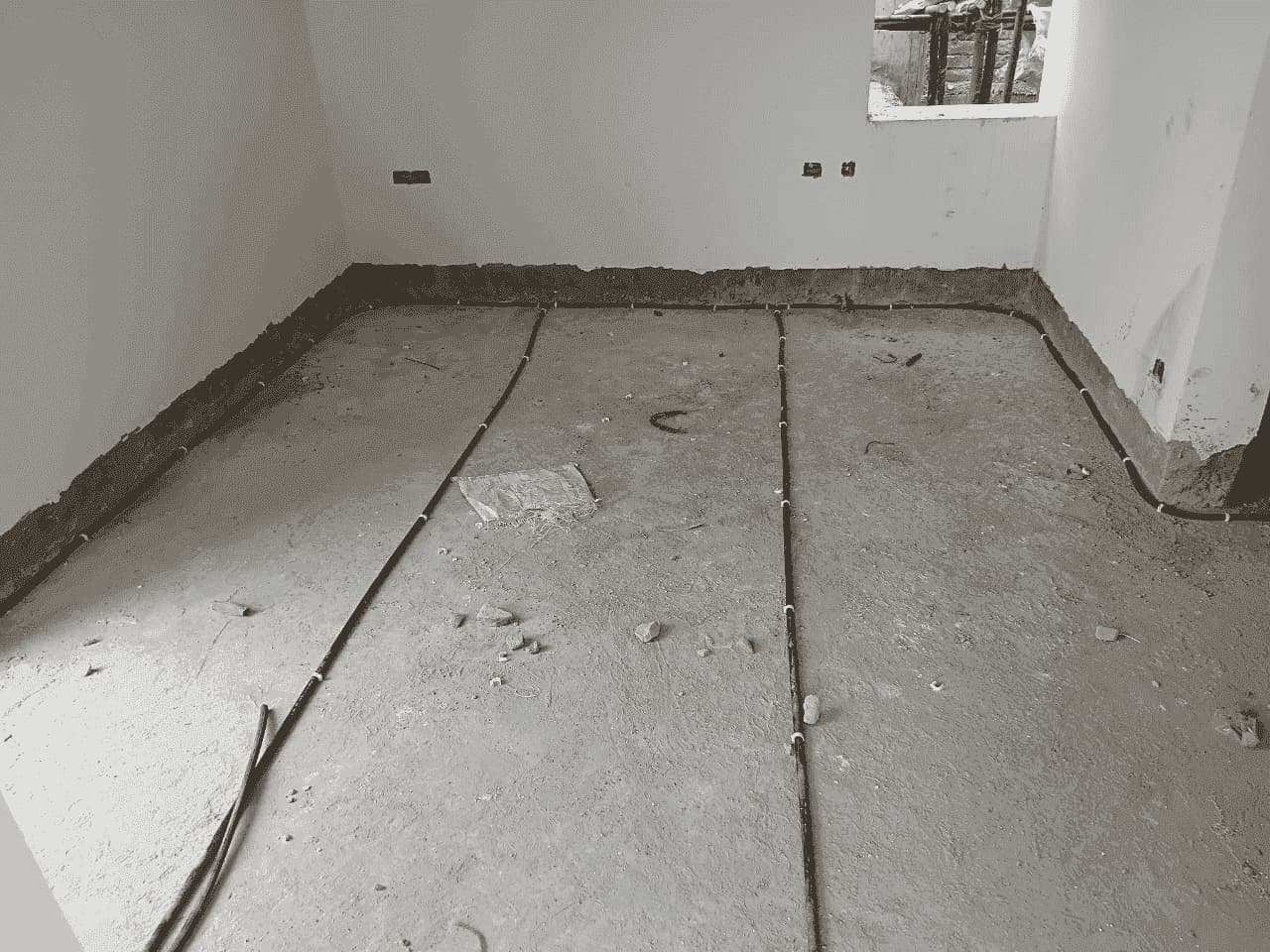 Black anti-termite pipes laid along the walls and across the floor of a room under construction